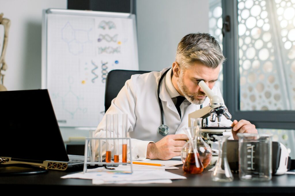 Senior Caucasian male scientist working with laptop, test tubes and flasks at the modern laboratory